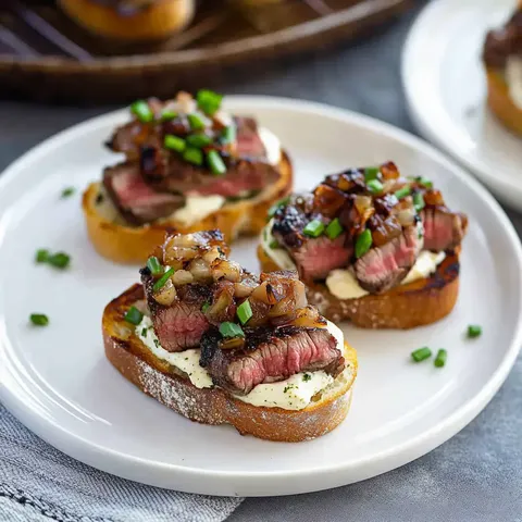 Ein Teller mit geröstetem Brot, belegt mit Steakstreifen, Meerrettichcreme, karamellisierten Zwiebeln und Frühlingszwiebeln.