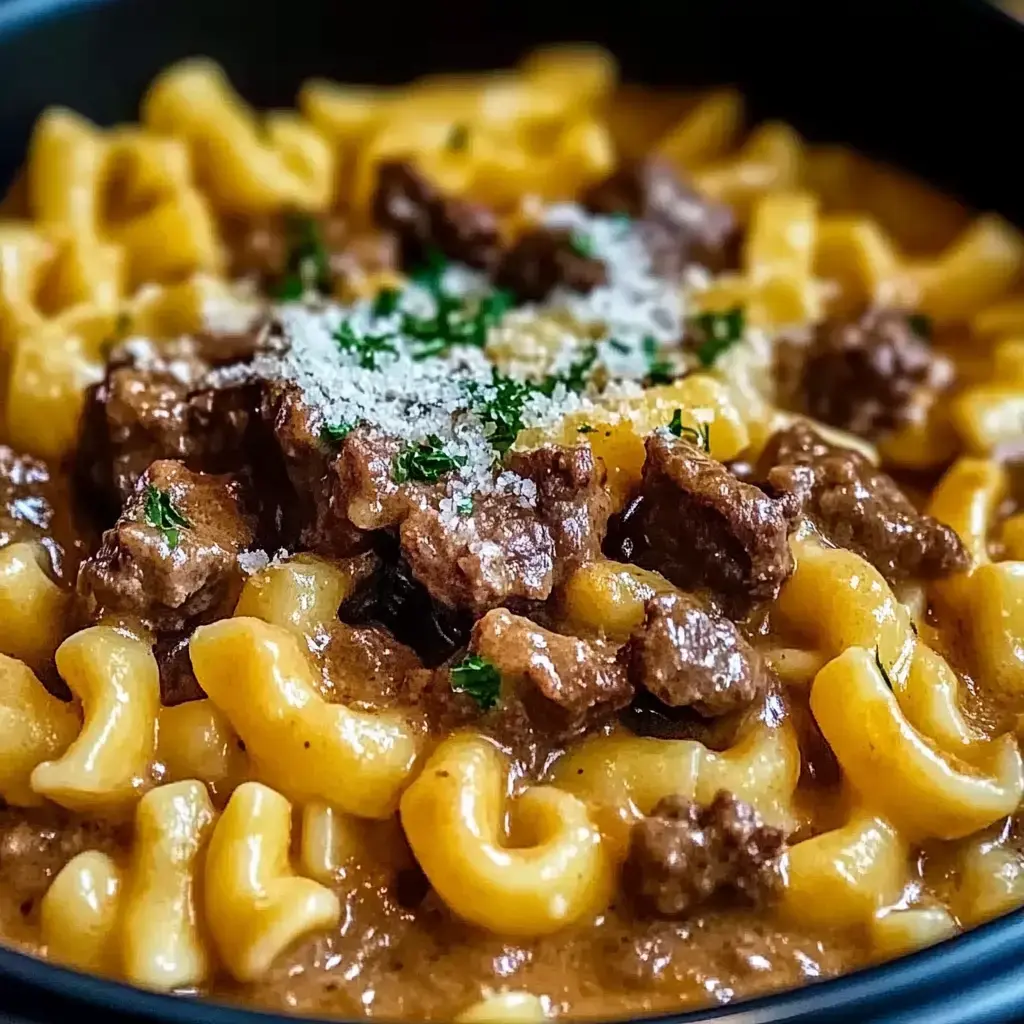 Nahaufnahme eines cremigen Pastagerichts mit lockigen Nudeln, zarten Rindfleischstücken, einer Prise geriebenem Käse und Petersilie.
