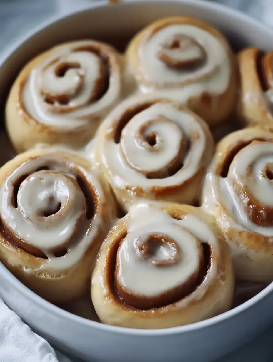 Weiße Auflaufform voll frisch gebackener Zimtschnecken mit viel Creme obendrauf.