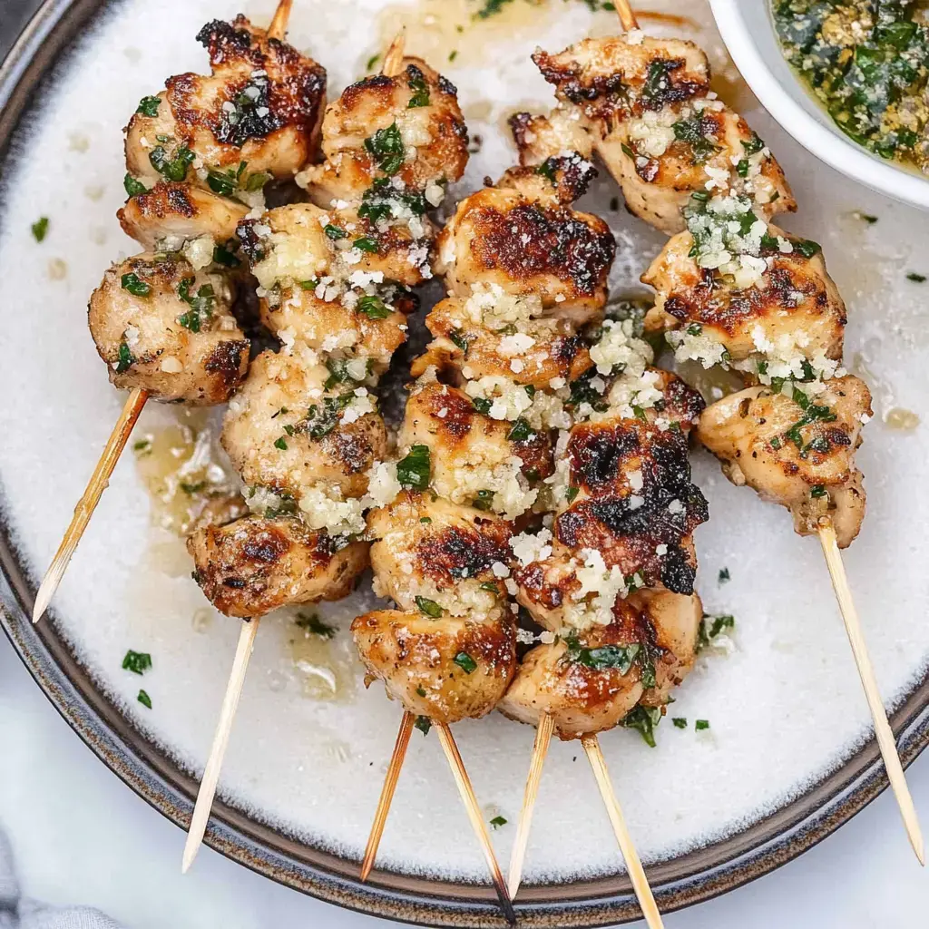 Gegrillte Hähnchen-Spieße mit Knoblauch und Kräutern auf einem Teller angerichtet, dazu eine kleine Schüssel grüne Sauce.