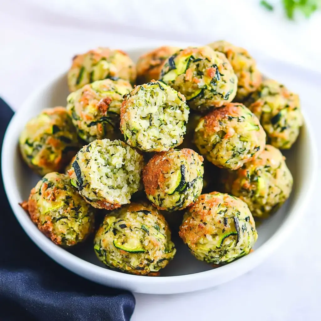Eine Schale voll goldbrauner Zucchinibällchen, einige angebissen, zeigen außen Knusprigkeit und innen grüne Gemüsestückchen.