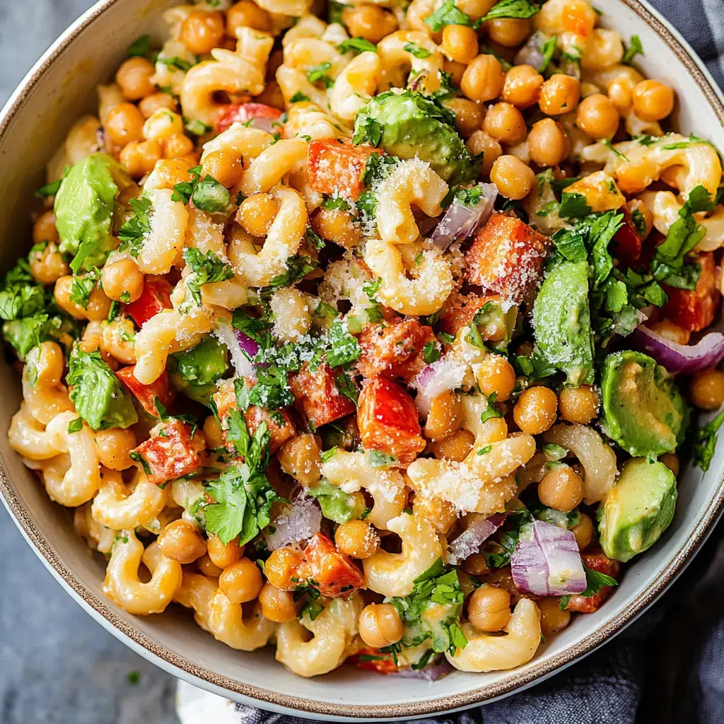 Eine bunte Bowl mit Makkaroni, Kichererbsen, gewürfelter roter Paprika, Avocado, roten Zwiebeln und frischen Kräutern, bestreut mit geriebenem Käse.