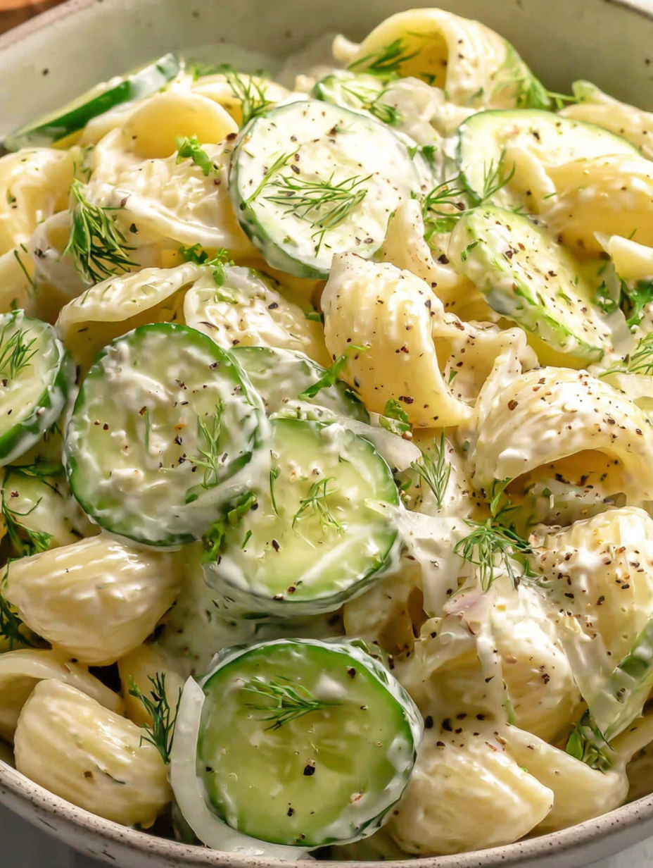 Eine Schüssel mit Pasta-Salat, Gurken und Käse.