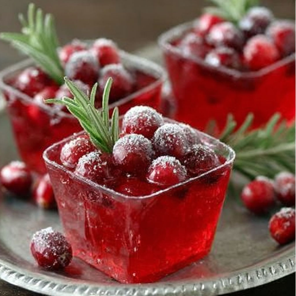Ein Teller mit roten Gelatine Shots und Preiselbeeren obendrauf.