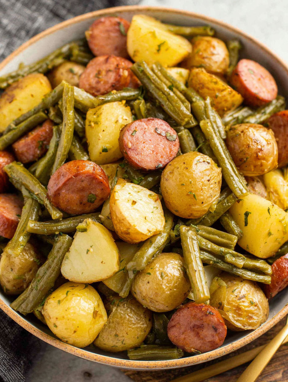 Ein Teller mit Kartoffeln, grünen Bohnen und Wurst.