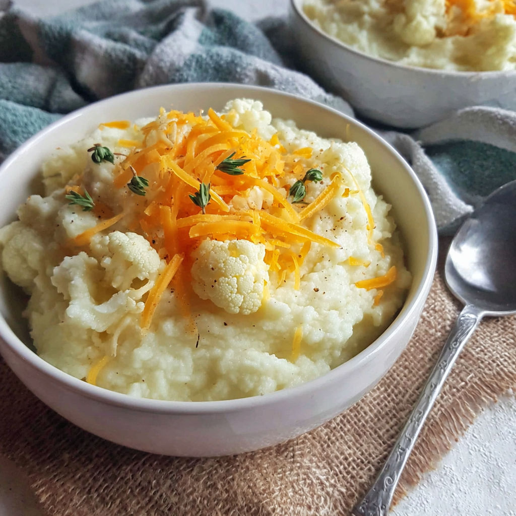 A bowl of mashed cauliflower with cheese on top.