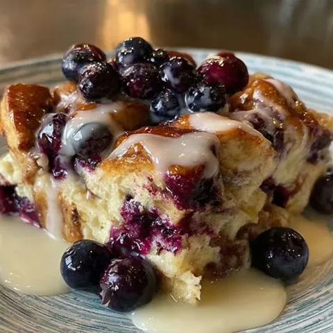 A blueberry cinnamon roll casserole with a dollop of cream on top.