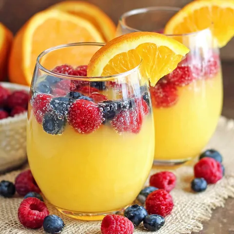 Zwei Gläser Ananas-Orangen-Bowle mit Blaubeeren und Himbeeren daneben.
