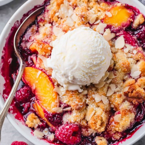 Eine Schüssel mit Pfirsich- und Himbeercobbler, darüber eine Kugel Eis.