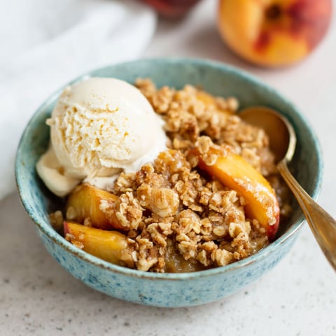 Eine Schüssel Pfirsichcrumble mit Eiscreme obendrauf.