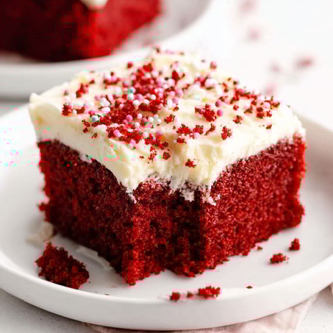 Ein Stück roter samt Kuchen mit weißem Frosting und Streuseln.
