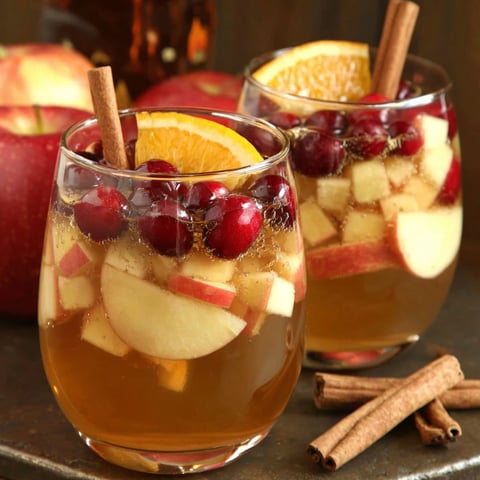 Two glasses of apple cider with cinnamon sticks in them.