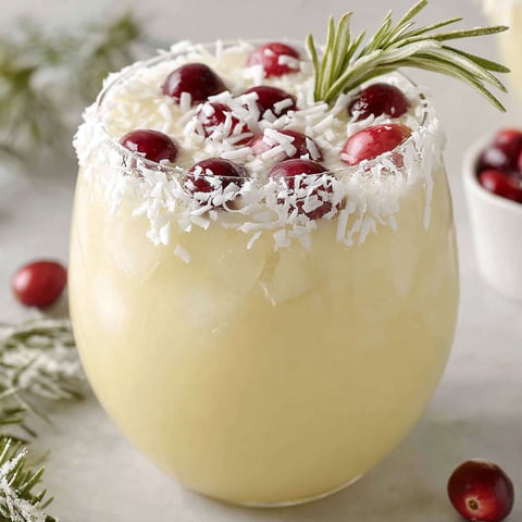 A glass of white Christmas punch with cranberries and pine needles.
