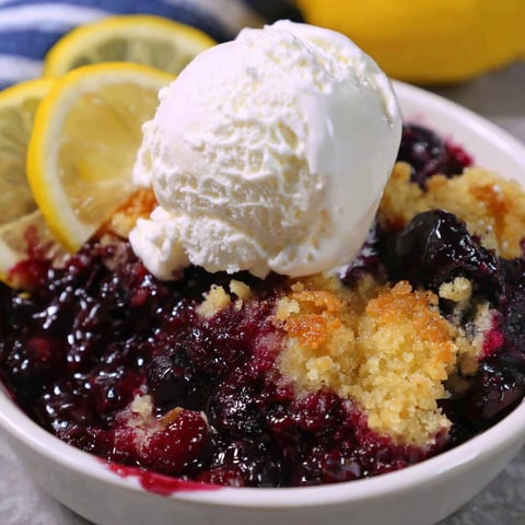 A bowl of lemon blueberry dump cake with a scoop of ice cream on top.