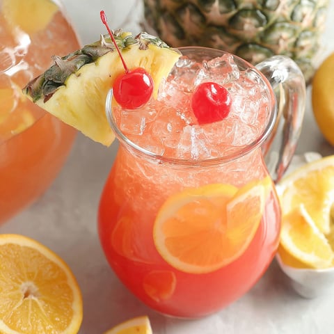 A glass of rum punch with a pineapple wedge and cherry on top.