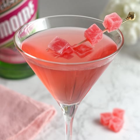 A pink starburst martini with a gold toothpick.