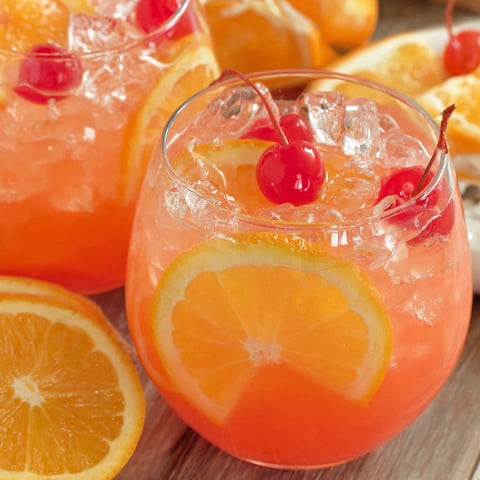 A glass of orange juice with a cherry on top.